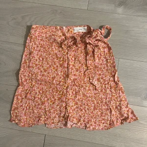 Blommig kortkjol med knytning - Söt blommig kortkjol från Mango i rosa och orange toner. 🌸Kjolen har en omlott-design med knytband i midjan och volangdetaljer längs nederkanten. Perfekt för varma sommardagar ☀️100% viskos. Använd fåtal gånger, jättefint skick. Rökfritt hem! Skriv meddelande vid frågor/fler bilder 🩷