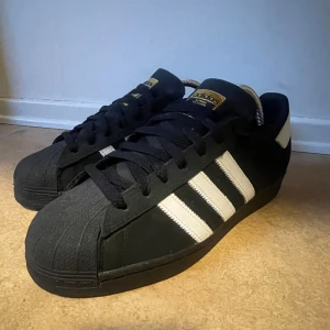 Svarta och vita Adididas sneakers - Säljer ett par klassiska svarta Adidas sneakers med vita ränder och logga. Skick 10/10 aldrig använda, storlek 8,5 uk, inget förutom skorna kommer med. Perfekta för en stilren look. Kan sänkas vid snabb affär.