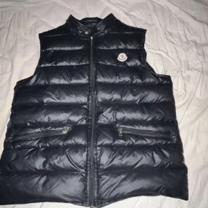 Svart dunväst från Moncler - Säljer en Moncler Väst. Säljer pågrund av att den är för liten. Perfekt nu får våren.