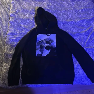 Svart hoodie med Tupac-tryck - Säljer en svart hoodie med ett stort tryck av Tupac på framsidan. Hoodien har en klassisk design med långa ärmar och en bekväm huva. Perfekt för dig som vill ha en stilren och cool look. 🖤