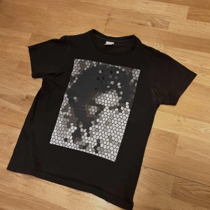 SS01 Number (n)ine mosaic t-shirt - Number (n)ine T-shirt från Spring-Summer 2001 kollektionen med ett mosaik tryck med Jeff Buckley. Size 1 motsvarar XS-S. Skicket är väldigt bra, inga tvättskador och tröjan har i princip inte töjts alls. Skicket går också att avgöras pga att hålen gjorda i produktionen är små. Säljer för att jag inte använder den. Priset är lägre för nöd i pengar.