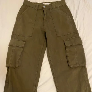 Olivgröna cargobyxor från Bershka - Snygga olivgröna cargobyxor från Bershka med flera praktiska fickor. Perfekta för en avslappnad stil. Byxorna har en normal passform och är tillverkade i bomull för extra komfort.