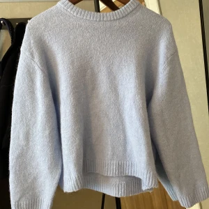 Ljusblå stickad tröja - Mysig ljusblå stickad tröja med ribbstickade muddar vid ärmslut och nederkant. Perfekt för kyliga dagar och ger en avslappnad look.