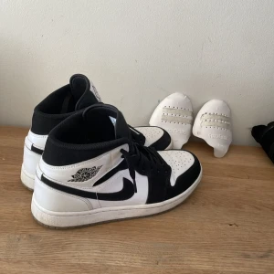 Svartvita Nike Air Jordans - Snygga svartvita Nike Air Jordans med klassisk design. Skorna har en hög siluett med snörning och den ikoniska swoosh-loggan på sidan. Perfekta för dig som vill ha en stilren look.