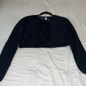 Mörkblå glittrig bolerotopp från Place - Snygg mörkblå bolerotopp från Place med glittrande detaljer. Perfekt för att lägga till lite extra stil till din outfit. Den är croppad och har långa ärmar.