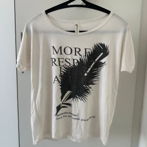 Vit t-shirt med tryck - Säljer en vit t-shirt med ett stort svart tryck av en fjäder och texten 'MORE RESPECT LESS ATTACK'. T-shirten har en rund halsringning och korta ärmar. Perfekt för en avslappnad stil.