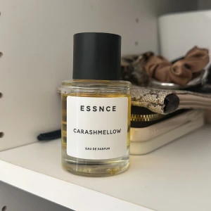 Essnce Carashmellow Eau de Parfum - Säljer en flaska Essnce Carashmellow Eau de Parfum. Flaskan är rund med en enkel och stilren design, genomskinlig med en svart kork. Parfymen har en gyllene färg som ger en lyxig känsla. Perfekt för den som älskar söta och mjuka dofter.