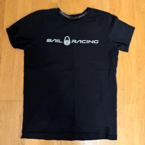 Svart t-shirt från Sail Racing - Snygg svart t-shirt från Sail Racing med tryck på framsidan. Perfekt för en avslappnad stil. Den har en normal passform och korta ärmar.
