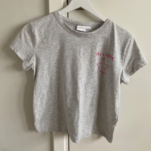 Grå t-shirt med rosa text - Säljer en grå t-shirt med korta ärmar och rosa texten 'MA CHÉRIE' samt en stjärna tryckt på både fram- och baksidan. Från Gina tricot💗