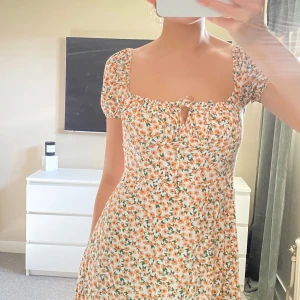 Blommig klänning med korta ärmar - Charmig blommig klänning med korta ärmar och knytning framtill. Klänningen har en söt volangdetalj och en lätt slits.