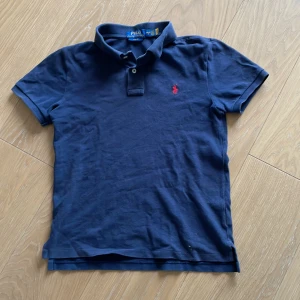 Mörkblå pikétröja från Ralph Lauren - Säljer en stilren mörkblå pikétröja från Ralph Lauren i slim fit. Tröjan har korta ärmar och en klassisk krage med två knappar. Den ikoniska röda loggan är broderad på bröstet. Perfekt för en avslappnad men ändå snygg look. Kontakta för frågor eller mer bilder 💯💯