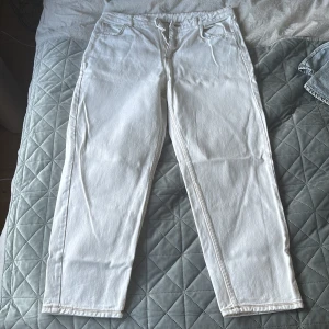 Vita jeansbyxor med brun etikett - Snygga vita jeansbyxor med en klassisk femficksdesign och en brun etikett baktill. Byxorna har en rak passform och stängs med dragkedja och knapp. Perfekta för en stilren look.