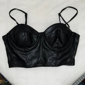 Svart korsett från Amisu - Snygg svart korsett från märket Amisu (butik New Yorker) i skinnimitation med justerbara axelband och dragkedja bak. Perfekt för en edgy look.