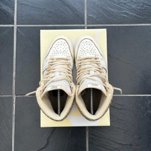 AIR JORDAN 1 Retro high OG craft  - Snygga Nike Air Jordans i en stilren beige färg med glittriga gulddetaljer. Skorna har snörning och en rund tå, vilket ger en klassisk look. Perfekta för dig som vill ha något unikt och trendigt.