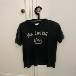 Svart t-shirt med tryck - Säljer en svart t-shirt med texten 'MA CHÉRIE' och en krona tryckt på framsidan. T-shirten har en avslappnad passform och korta ärmar. Perfekt för en casual look! Storlek 158-164 men passar xs💗