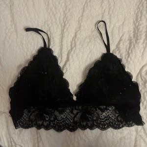Svart spets bh - Snygg svart bralette med spetsdetaljer och smala axelband. Perfekt för att lägga till en touch av elegans under dina kläder. Den har en vacker spetskant som ger en feminin känsla.
