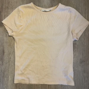 Ljusrosa ribbad t-shirt från KappAhl - Säljer en stilren ljusrosa ribbad t-shirt från KappAhl. Den har en klassisk rund hals och korta ärmar, perfekt för en avslappnad look. Passar bra till både jeans och kjol. Perfekt för vår och sommar! Den har används mycket men väl omhändertagen. (Den har en gul liten fläck på framsidan som man kan se på sista bilden, alltså bild fem) Skönt material och supefin!🩷