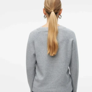 Ljusgrå stickad tröja från Vero Moda - Mysig ljusgrå stickad tröja från Vero Moda med rund halsringning och långa ärmar. Tröjan har en enkel och clean design med ribbade muddar vid ärmslut och nederkant. Perfekt för lager-på-lager och chill vardagsstil.