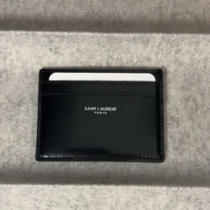 Ysl korthållare  - Ysl plånbok/korthållare Ny, aldrig använd. Medföljer certifiering av äkthet. Glansig svart färg. Ny pris runt 3000kr
