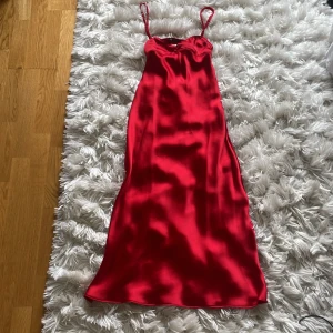 Röd satinklänning från Zara - Snygg röd långklänning från Zara i glansig satin med smala, tvinnade axelband och en lätt v-ringad urringning. Klänningen har en figurnära passform och öppen rygg med fina detaljer. 