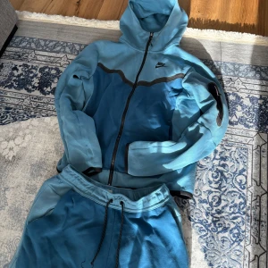 Blå tracksuit från Nike - Säljer  blå tracksuit från Nike med cool tvåfärgad design och svarta detaljer. Byxorna har resår i midjan med snörning och sidofickor. Perfekta för chill eller träning, matchar med hoodie för en komplett look.