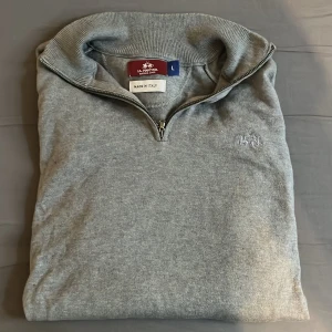 Grå half zip tröja från La Martina - Snygg grå tröja från La Martina med half zip och hög krage. Tillverkad i Italien och har diskret broderad logga på bröstet. Långärmad modell i mjukt material, perfekt för lager-på-lager och chill stil. Hör av er vid minsta lilla fråga. Ny pris: 2300kr 