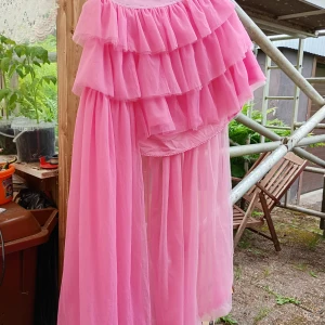 Rosa volangklänning/kjol från SHEIN XL - Superfin långklänning /kjol starkt rosa från SHEIN med flera lager volanger upptill och flowy, transparent kjol. Klänningen har rund halsringning och är ärmlös, perfekt för dig som vill sticka ut med en färgglad och lekfull look. Mäter hela 107 cm från resåret och neråt.