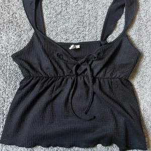 Svart linne från Nelly - Supersnygg svart topp från Nelly med volang axelband och knytning framtill. Sydde upp axelbanden lite då de var för långa för mig (se sista bilden), men det är lätt att sprätta upp om man vill ha dem långa. Säljer då den tyvärr är för liten för mig. Aldrig använd💞