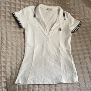 Vit Moncler piké med broderad logga - Vit pikétröja från Moncler med klassisk krage och knäppning framtill. Såklart äkta! Storlek 164 barn men passar även xs dam