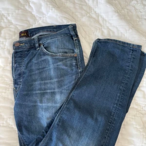 Lee Daren Button jeans blå W36 L30 - Snygga blå Lee Daren Button jeans i klassisk rak modell. Tillverkade i ekologisk bomull med fem fickor, tydliga kontrastsömmar och Lee-logga på bakfickan. Perfekta för dig som gillar en tidlös jeanslook.