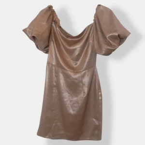 Champagnefärgad kort klänning med puffärm - Superfin kort klänning i skimrande champagnefärg med stora puffärmar och snygg draperad urringning. Tillverkad i glansigt material som ger en lyxig känsla. Dragkedja bak för enkel påklädning. Perfekt för dig som vill sticka ut.