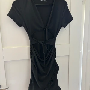 Svart kort klänning  - Svart kort klänning från SHEIN med v-ringning, snörning framtill och snygga cut-outs i midjan. Klänningen har korta ärmar, rynkade detaljer och en draperad kjol