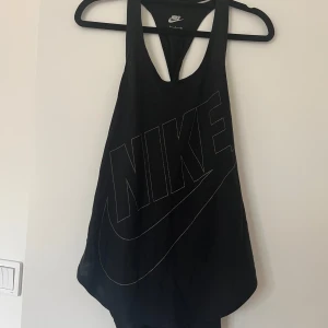 Svart linne från Nike - Säljer ett svart linne från Nike med stort logotryck framtill. Modellen är loose fit med djupa ärmhål och brottarrygg, perfekt för träning eller chill. 