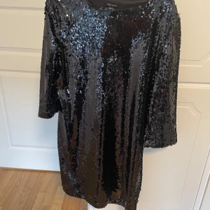 Svart glittrig paljettklänning Esmara - Svart kortklänning från Esmara täckt med glittriga paljetter. Klänningen har halv-långa ärmar och en rak, loose passform. Perfekt för dig som vill sticka ut med en riktigt glittrig look. Snygg till sneakers eller klackar!