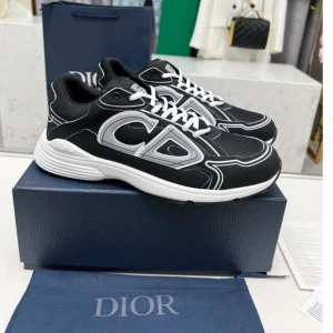 Svarta Dior sneakers med vita detaljer - Snygga svarta sneakers från Dior med vita och silverfärgade detaljer samt tydlig CD-logga på sidan. Skorna har vit platt sula, snörning och är tillverkade i en mix av textil och syntet. Perfekta för dig som vill sticka ut med en exklusiv och modern look.