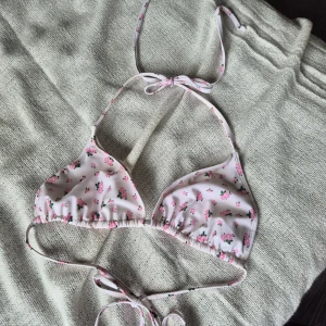 Blommig trekantsbikini från Nelly - Supersöt oanvänd trekantsbikini från Nelly i vitt med små rosa blommor och gröna blad. Klassisk modell med knyt i nacken och ryggen 🌸säljer pga att den inte passade mig, skriv vid frågor🌸