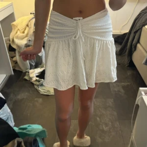 Vit kort kjol med snörning och volang - Superfin vit kort kjol med broderade detaljer och volangkant. Kjolen har insydda shorts