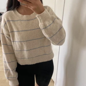 Beige randig stickad tröja Shein - Supermysig beige stickad tröja från Shein med tunna blå ränder. Tröjan har en croppad passform, rund halsringning och långa ärmar med breda muddar. Perfekt för lager-på-lager och chill dagar.