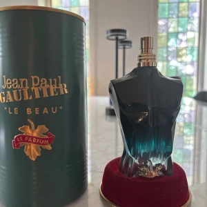Jean Paul Gaultier Le Beau Parfym endast flaska (Tom) - Jean Paul Gaultier Le Beau Le Parfum i en unik flaska formad som en manlig överkropp i mörkblått glas med gulddetaljer. Kommer med original grön metallburk och röd sammetsbas. Det är inget kvar i den men Bra om man vill samla på parfym.