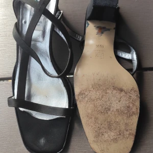 Svarta sandaler med smala remmar - Stilrena svarta sandaler med smala remmar som korsar foten. Snygg silverfärgad innersula och platt sula. Perfekta för varma dagar och ger en elegant look till din outfit.