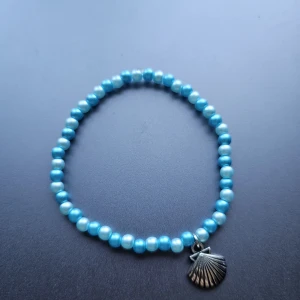 Blått pärlarmband med snäckberlock - Superfint armband med små blå pärlor och en silverfärgad snäckformad berlock. 