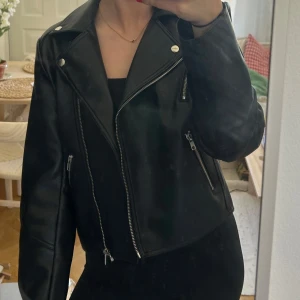 Svart skinnjacka från Bik Bok - Snygg svart skinnjacka från Bik Bok. Jackan har silvriga dragkedjor och bred krage. Modellen är croppad och har lång ärm ⭐️