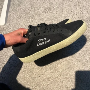 Svarta Saint Laurent sneakers - Svarta sneakers från Saint Laurent med vit broderad logga på sidan. Skorna är perfekt nu till sommaren och nästan. Helt nya, kom dm vid frågor