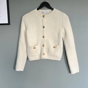 Beige stickad kofta från Zara - Superfin beige stickad kofta från Zara med snygga guldknappar framtill och två fickor. Den har en liten fläck på lappen (se bild) men syns inte när den används, perfekt till lite kyligare dagar eller kvällar.