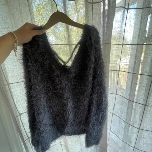 Mörkgrå fluffig stickad tröja - Supermjuk och fluffig mörkgrå stickad tröja med v-ringning. Materialet är lurvigt och ger en cool, trendig look. 
