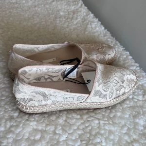 Beige spetsiga espadrillos från Zara - Snygga espadrillos från Zara i beige med vacker spets och blommigt mönster. Skorna har platt sula med klassisk flätad kant och rund tå. Perfekta för en somrig och avslappnad look.