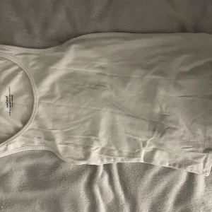 Vit ribbad linnetopp från H&M - En klassisk vit ribbad linnetopp från H&M med rund halsringning och ärmlös design. Perfekt att styla till jeans eller shorts för en enkel och clean look. Materialet är mjukt och stretchigt för extra komfort.