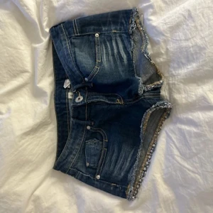 Mörkblå jeansshorts med fransar - Snygga mörkblå jeansshorts med slitna detaljer och fransig kant. Klassisk femficksmodell med knapp och dragkedja framtill. Perfekta för varma dagar och ger en cool, avslappnad vibe.