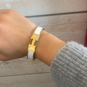 Hermens vit och guld armband - Säljer ett Hermens Clic H-armband i vit med gulddetaljer. Fint skick och knappt använt.