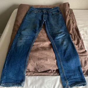 Blå raka jeans i klassisk modell - Säljer ett par klassiska blå jeans med raka ben och normal passform. Jeansen har fem fickor, dragkedja och knapp framtill samt snygga slitningar för en avslappnad look. Perfekta till sneakers eller boots.
